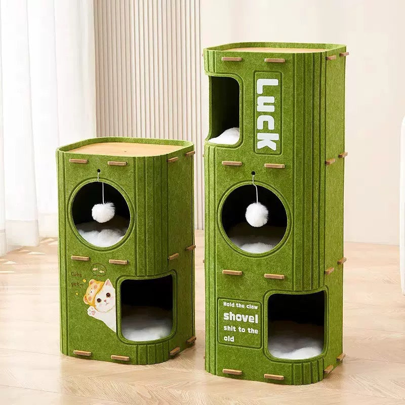 A modern, cylindrical cat tree tower made of green felt material, measuring 60cm in height and 37cm in width and depth. It features multiple levels including a top platform where a ginger cat is lounging, a middle circular window with a hanging white pom-pom toy, and a bottom arched entrance with a soft cushion. The front panel is decorated with a cute cartoon cat decal reading 'Cute pet'. Dimensions: 60cm (H) x 37cm (W) x 37cm (D). Cat not included.