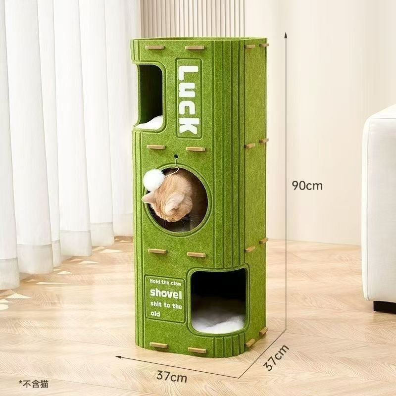 A modern, modular cat tree tower made of sturdy green felt. This 90cm tall furniture features a vertical 'LUCK' logo, wooden climbing pegs on the sides, a cozy circular window with a hanging pom-pom toy, and an open cubby at the base with a soft cushion. Dimensions: 90cm (H) x 37cm (W) x 37cm (D).